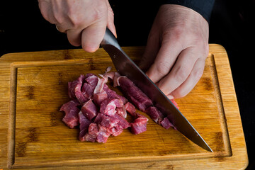 hands of the chef cut meat on the black table