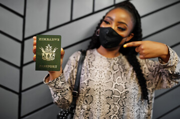 African woman wearing black face mask show Zimbabwe passport in hand. Coronavirus in Africa...