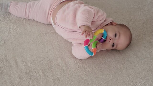 infant, childhood concept - close-up of smiling happy plump funny brown-eyed chubby face of newborn kid awake. toothless 7 month baby grimaces, closes eyes lie on soft bed in pink with teether at home