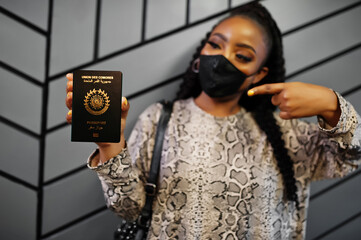 African woman wearing black face mask show Comoros passport in hand. Coronavirus in Africa country, border closure and quarantine, virus outbreak concept.