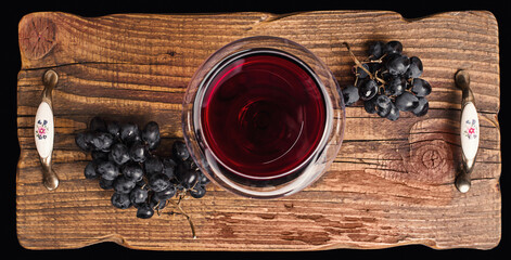 Red wine in a glass and ripe grapes on rustic textured wooden tray.