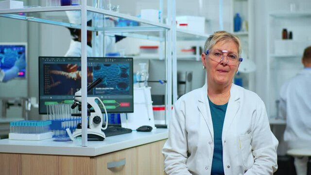 Portrait of senior scientist woman looking at camera in modern equipped lab. Multiethnic team examining virus evolution using high tech and chemistry tools for scientific research, vaccine development