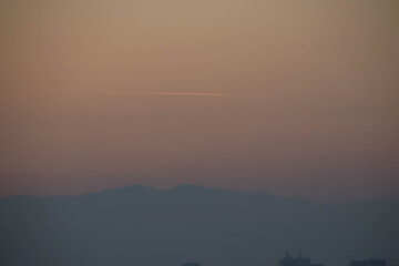 Close up of a sunset golden sky with a trace of the airplane and the hill.