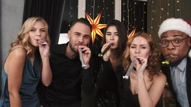 Group of friends blowing party blowers. CHristmas or new year celebration in a circle of friends.