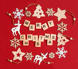 Creative Christmas flat lay composition, inscription Merry Christmas made of wooden blocks with letters and Xmas decorations arranged in square frame on bright red background.Snowflakes, deers, stars.