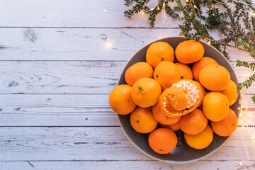 top view on a bowl of ripe orange tangerines on a white wooden table, christmas lights and christmas tree in background, copy space - 395140934