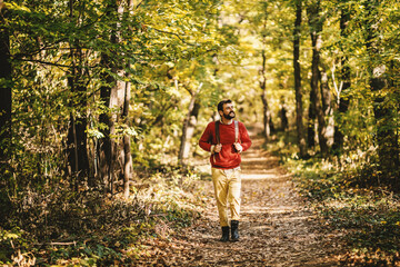 Full length of young bearded cheerful explorer walking in the forest on a beautiful autumn day. Man...