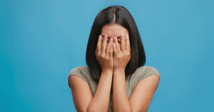 Studio portrait of displeased crying young asian woman, feeling stress, depression and failure, blue background