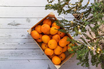 a box of ripe orange tangerines on a white wooden floor under a christmas tree, healthy present from santa, with copy space - 395141917