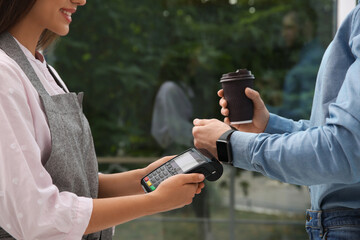Man using smart watch for contactless payment via terminal in cafe, closeup