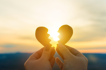 Two hands hold a broken heart on the background of the sunset. Concept spat divorce dissolution,...