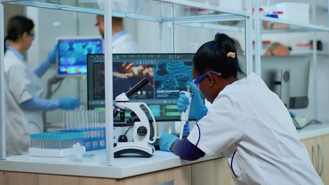 Black woman chemist analysing reaction of virus on microscope in laboratory. Multiethnic team examining vaccine evolution using high tech for scientific research, treatment development against covid19