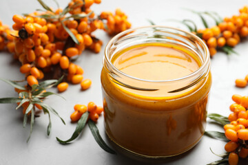 Delicious sea buckthorn jam and fresh berries on light grey table