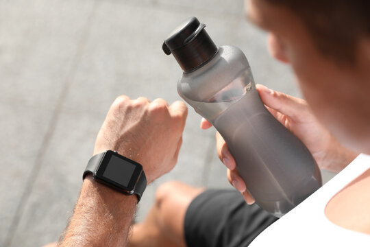 Man with bottle of water checking fitness tracker after training outdoors, closeup - Powered by Adobe