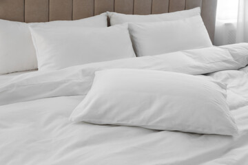 Many soft pillows and blanket on large comfortable bed indoors