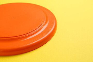 Orange plastic frisbee disk on yellow background, closeup. Space for text