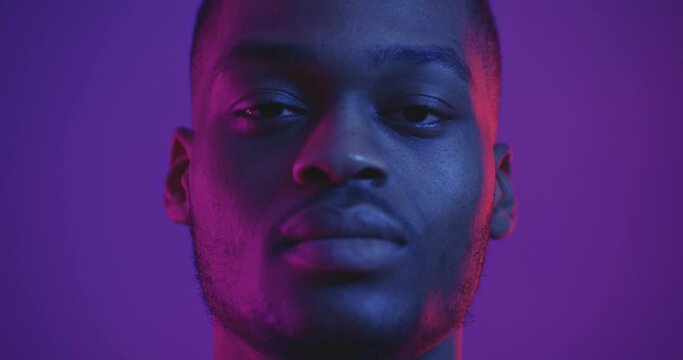 Close up portrait of handsome african american man raising face to camera in neon lights, slow motion