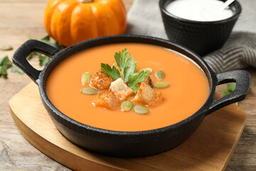 Tasty creamy pumpkin soup with croutons, seeds and parsley in bowl on wooden table