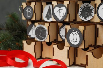 Wooden advent calendar and red ribbon on white table, closeup