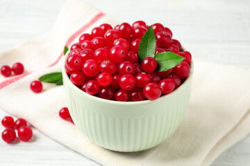 Tasty ripe cranberries and green leaves on white table, closeup