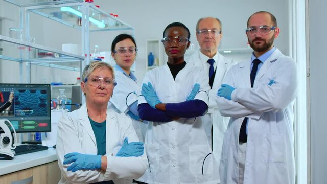 Professional multiethnic medical staff looking at camera in modern equipped lab. Team of doctors examining virus evolution with high tech, chemistry tools for scientific research, vaccine development
