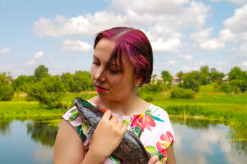 A smiling woman in a pink dress holding a large brown flathead catfish. 