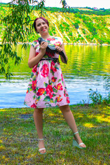 A smiling woman in a pink dress holding a large brown flathead catfish.