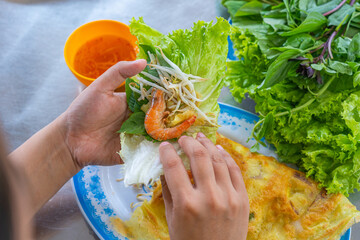 Woman's hands wrapping food with lettuce while eating Banh Xeo 