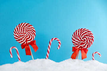 Christmas red candy canes and lollipops in snow on blue background. Merry Christmas sweets and Happy New Year concept