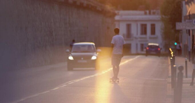 Young man skateboarding down the street in Montpellier in slowmotion , riding in the street, cruising home in the city during the sunset