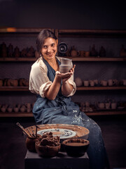 Beautiful young and cheerful woman shows how to work with clay and pottery wheel. Handiwork.