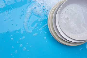 Washing dishes concept. Wet blue with soapy foam background.