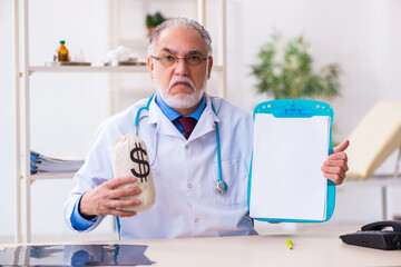 Old male doctor holding moneybag in the hospital