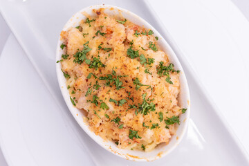 Overhead view of lobster macaroni and cheese served hot in a casserole plate topped with fresh basil