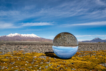 The Central Plateau snow capped volcanoes in the Desert road reflected in a crystal ball sitting on...