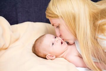 Natural Portrait of Young Caucasian Mother Kissing Her Newborn Baby Boy Lying on Bed.