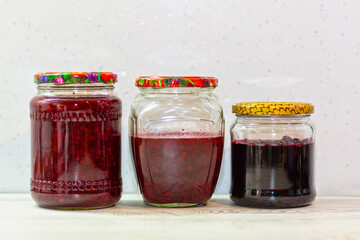 There are three jars of jam on a white table, homemade preparations for the winter, lingonberry jam, black rowan jam