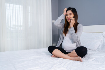 stressed pregnant woman talking on a mobile phone in bed