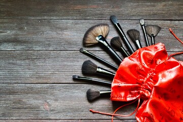 Makeup brushes in red bag on wooden background. Top view, copy space. Xmas, happy new year, female wishes concept.