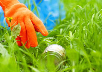 Iron garbage lying on the grass is picked up by the hand of a volunteer in a bright glove. Sorting...