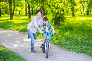 Mom helps the child learn to ride a bike on a bike ride in the park. Family weekend getaway concept