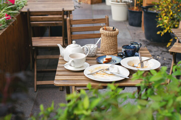 dirty white dishes on wooden table with cutlery in cafe on street without people