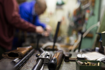 Closeup of disassembled shotgun during repair or maintenance on worktable of gunsmith in professional weapons workshop. Selective focus on gun