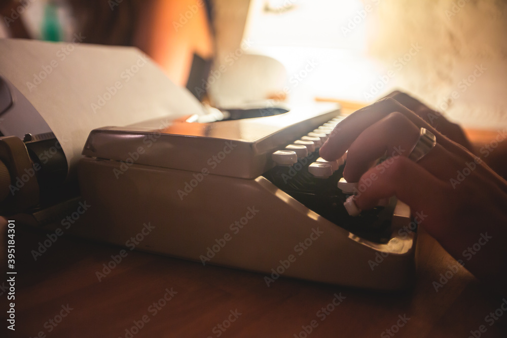 Fototapete Process of writing a text letter on a white sheet of paper with old-fashioned typewriter, modern writer machine in warm room light, close up view of hands writing and printing