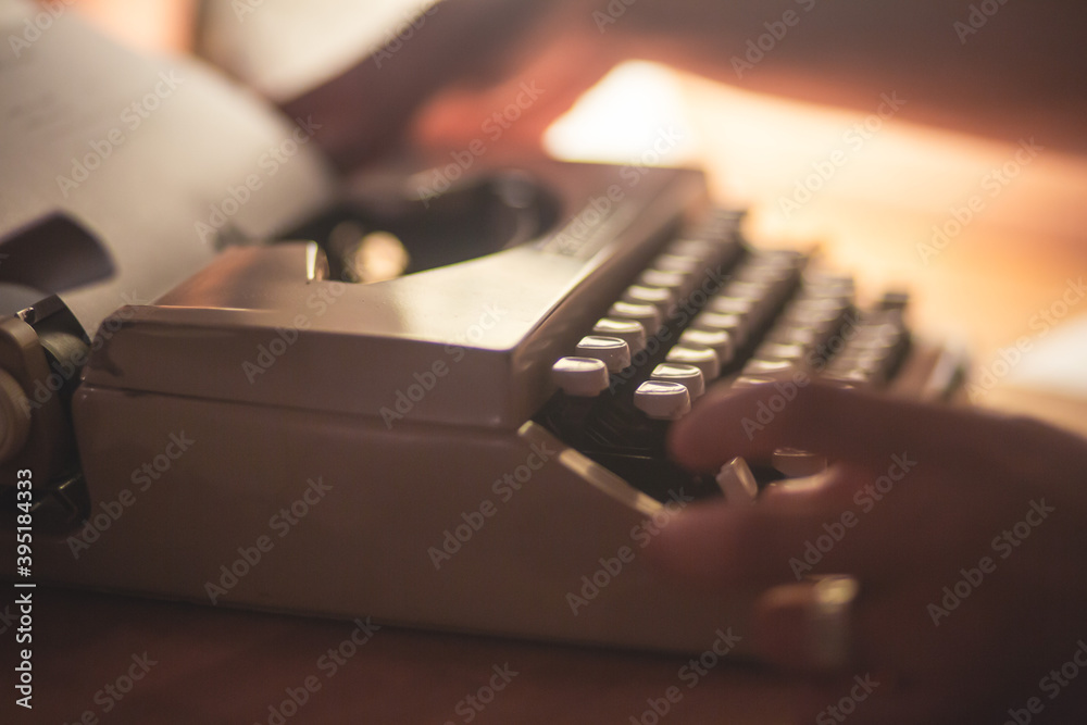 Fototapete Process of writing a text letter on a white sheet of paper with old-fashioned typewriter, modern writer machine in warm room light, close up view of hands writing and printing