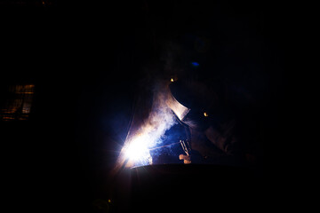 A welder is welding a metal pipe with electric welding. Electric welder repairs a pipe in a workshop