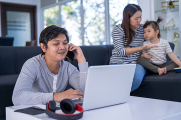 Young working father work from home while babysitting his playful daughter at home. Working father Phone calls with customers  and daughter playing beside.
