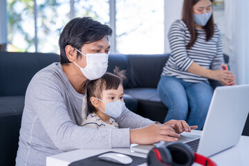 Happy family wearing a face mask. Young working father work from home while babysitting his playful daughter at home. Working father and daughter playing beside.