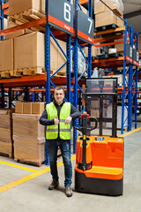 Storehouse employee in uniform working on forklift in modern automatic warehouse. Worker showing thumbs up. Boxes on the shelves of the warehouse. Warehousing, machinery concept. Logistics in stock.