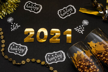 2021 made with golden numbers, glasses with golden balls and stars, confetti and ornaments on black background. New Year decoration